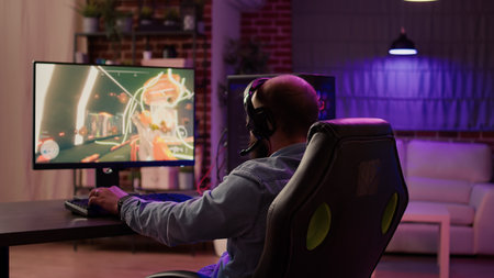 Over shoulder view of man playing online action game congratulates team on headset after celebrating...