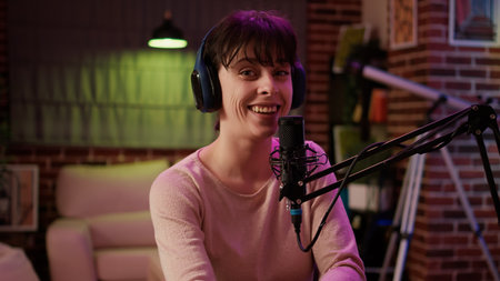 Portrait of woman with headphones talking energetic in online radio show using microphone and professional recording equipment. Famous influencer recording entertainment podcast in home studio.の写真素材