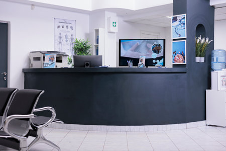 Facility registration counter in waiting area lobby, computer to make checkup appointments with healthcare report papers. Empty hospital reception desk with medical forms and insurance support.の写真素材