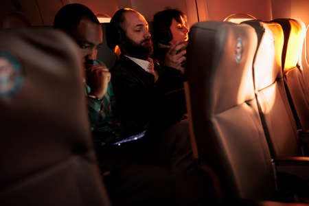 Diverse passengers flying in economy class with airplane jet, using international airways service on commercial flight. Group of people travelling by plane to go to holiday destination or job trip.の写真素材