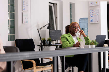 Office manager having conversation with clients on landline phone, working in start up company...