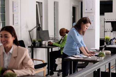Startup company employee working on laptop on research, concentrated office manager standing near workplace desk. Worker looking at financial data on computer in coworking spaceの写真素材