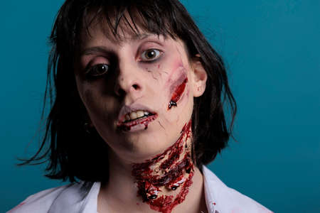 Portrait of creepy zombie woman with scratches, acting dangerous and cruel. Sinister apocalyptic brain eating monster having bloody scars and wounded face with blood. Close up.の写真素材