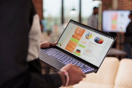 Employee holding laptop with business diagrams in company office, management presentation of diagrams and graphs on computer screen. Data report and research information on pc. Close up.の写真素材