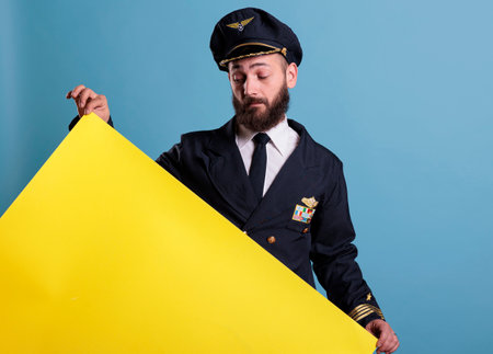 Airplane pilot holding yellow empty advertising banner with copy space, aviator looking at blank...