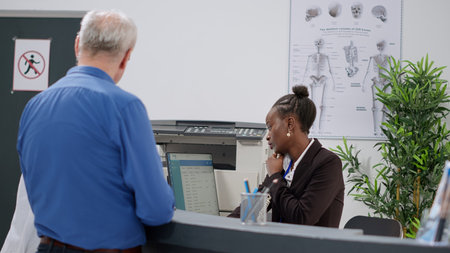 African american receptionist talking on landline phone call, making medical appointments and...