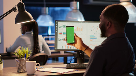 Company employee holding mobile phone with greenscreen in business office. Analyzing blank mockup...