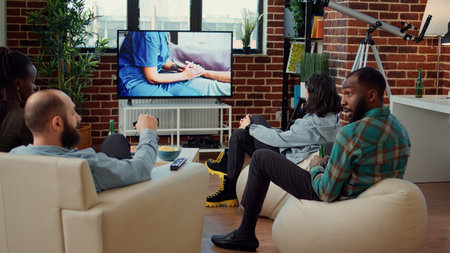 Multiethnic group of people watching drama tv series at house party with beer bottles and snacks....