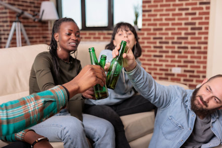 Men and women doing cheers gesture and clinking glass bottles of beer, toasting for friendship reunion at fun gathering. Cheerful people doing toast with alcoholic beverage, leisure activity.の写真素材
