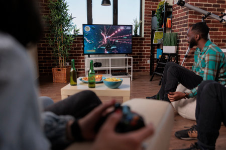 Men and women using tv console and joystick to play video games, having fun at house gathering with beer bottles. Group of people enjoying shooting competition with gaming strategy.の写真素材
