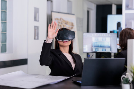 Architect working on project blueprints wearing vr helmet in architecture office. Employee engineering and using virtual reality headset, real estate agency worker in ar goggles.の写真素材