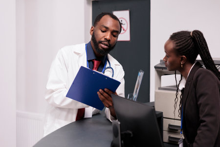 African american team working on checkup reports at hospital reception desk, analyzing patients appointments on papers. Doctor and receptionist using medical forms to help people with disease.の写真素材