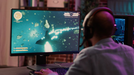 Over shoulder view of gamer streaming fast paced space shooter action game on gaming pc. Man playing...