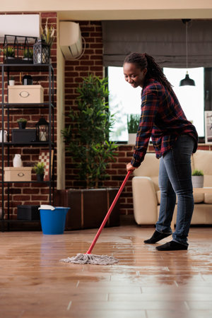 African american woman mopping the floor at home, doing housework on saturday morning. Housewife...