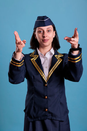 Smiling flight attendant showing emergency exit on plane board, safety instruction demonstration. Stewardess in professional uniform pointing with fingers at camera front viewの写真素材