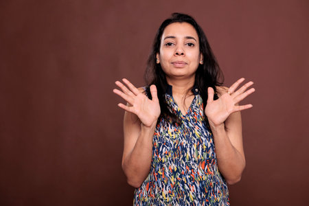 Smiling indian woman showing no problem gesture with palms, looking at camera with positive facial expression. Young lady standing with spread arms portrait, front view studio medium shotの写真素材