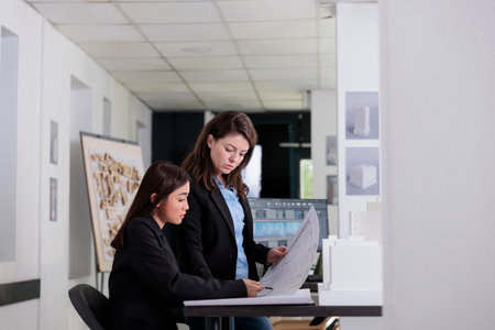 Architects holding blueprint, discussing construction project sketch, working with drafts in coworking space. Employees in architecture office at workplace desk, engineers looking at plan layoutの写真素材