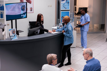 Young adult filling in registration form at hospital reception desk, writing medical checkup report before attending appointment. Woman checking papers in facility lobby, having consultation.の写真素材