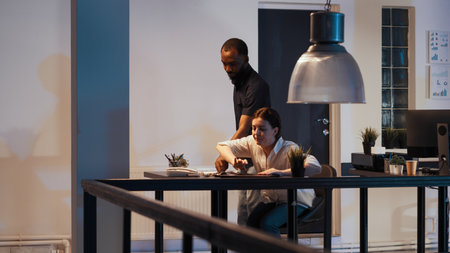 Female freelancer leaving startup office late at night, going home with colleague. Working after hours on professional report and corporate online presentation, planning documents.の写真素材