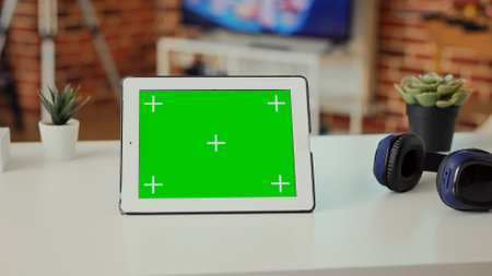 Empty desk with digital tablet showing green screen on display, used to work on modern technology at home. Isolated mockup template and chroma key background with copyspace screen on wireless device.の写真素材