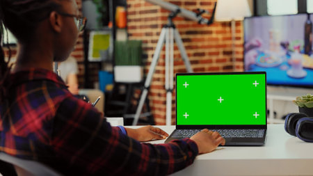 African american worker using greenscreen template on laptop, sitting at desk to check isolated display with chroma key. Looking at blank background with mockup copy space on portable pc.の写真素材