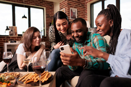 Young african american couple showing photos on cell phone screen to different ethnicities women, everyone smiles. Multicultural group friends sitting, looking mobile, smiling, talking, discussing.の写真素材