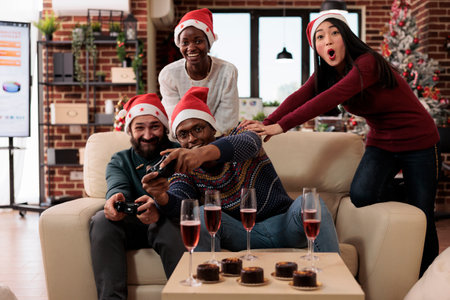 Festive work colleagues playing online video games to celebrate christmas eve at office party with holiday decorations. People enjoying gaming competition during xmas winter festivity.の写真素材