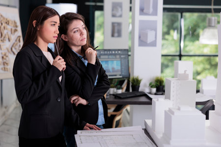 Thoughtful architects discussing 3d building printed model, working on construction design project. Architecture designers thinking, real estate workers cooperation in coworking spaceの写真素材