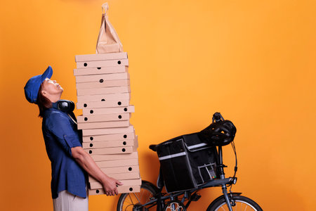 Senior takeaway delivery standing with giving food order and holding pizza boxes, pizzeria service. Restaurant courier transporting takeout food with bike on yellow background. Takeout conceptの写真素材