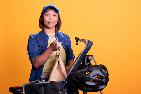 Takeaway food delivery worker wearing pizzeria uniform while delivering food order to client during lunch time. Asian restaurant employee using bike as transportation. Takeout service conceptの写真素材