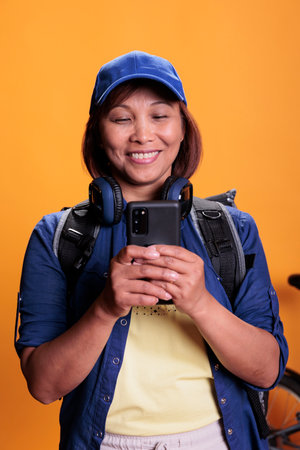 Asian food delivery employee checking customer address on mobile phone in studio with yellow...