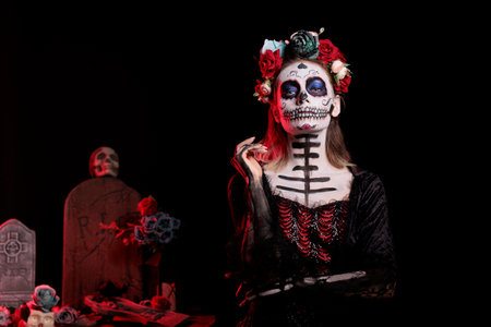 Spooky lady of death with black costume and catrina skull body art, wearing flowers headband with roses. Celebrating dios de los muertos mexican tradition on halloween in studio.の写真素材