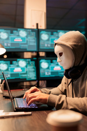 Scary male scammer wearing mask hacking database servers, hacker with hood breaking into computer...