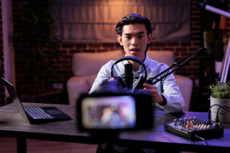 Asian vlogger broadcasting product review with headset on social media channel, recording online vlog and talking about audio headphones. Filming recommendation video with livestreaming station.の写真素材