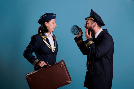 Stewardess and airplane pilot running late at airport, holding retro alarm clock, carrying baggage. Flight attendant and aircraft captain overslept, looking at time, hurry up at work with luggageの写真素材