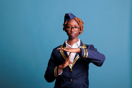 African american female flight attendant making time-out gesture with hands in T-shape, expressing need to rest from work. Serious woman announcing pause symbol with palms, studio shot.の写真素材