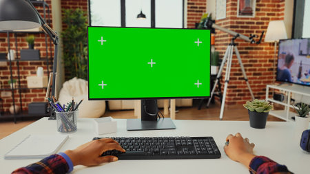 Office worker analyzing isolated greenscreen on computer to work with chroma key display on monitor. Looking at blank copyspace and mockup to use keyboard and desktop. Tripod shot.の写真素材