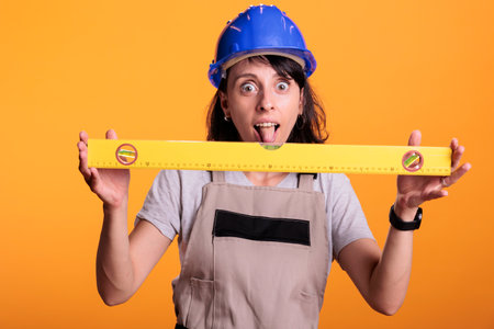 Cheerful construction worker using leveler to check flat walls, working on building and...