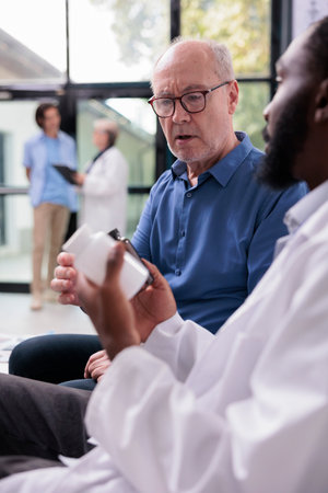 African american physician explaining medication treatment to senior patient while showing...
