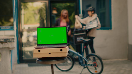 Laptop showing greenscreen display outdoors, food delivery service at front door. Running isolated chroma key template with blank mockup and copyspace background on computer screen.の写真素材