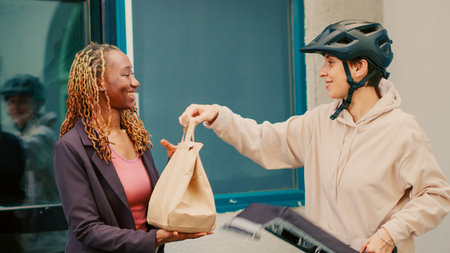 Fastfood courier delivering takeaway meal in paperbag to african american client, giving package...