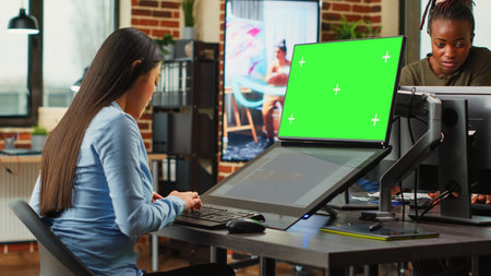 Creative agency employee looking at greenscreen and 3d developing software on touchscreen monitor. Working with isolated chroma key display and using game infographics, copyspace. Tripod shot.の写真素材