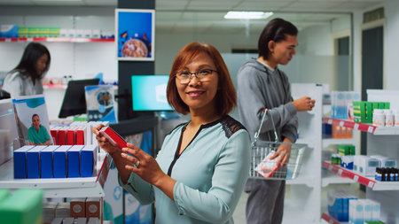 Asian woman searching for medicaments in pharmacy shop, looking at shelves filled with pills boxes and bottles. Drugstore client reading medicine packages, pharmaceutical products.の写真素材
