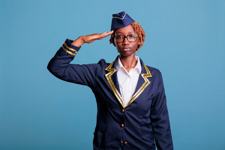 Portrait of female airline stewardess waving dressed in airline uniform. African american woman...