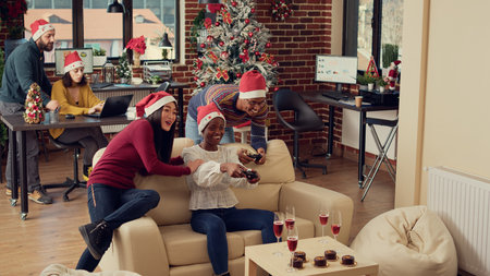 Cheerful colleagues playing video games at christmas party in office, feeling happy and enjoying winter holiday celebration. Using controllers on console to play gaming competition at festivity.の写真素材