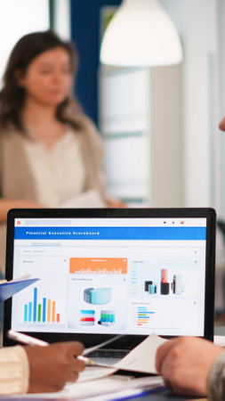 Busy multicultural, diverse employees analysing annual financial statistics sitting at desk in front of laptop holding documents searching business solutions. Team of businesspeople working in companyの写真素材