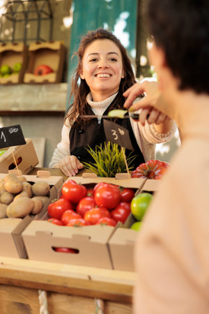 Smiling friendly organic fruits and vegetables shop owner offering customer to taste different varieties of apples at food market. Positive female farmer selling fresh local homegrown productsの写真素材