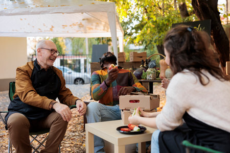 Group of cheerful people tasting food and wine at food fair, sitting together at table and having...