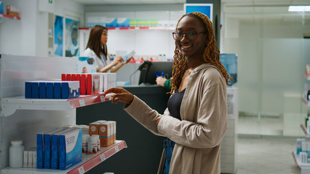 African american smiling woman checking packages of medicaments on drugstore shelves, buying...