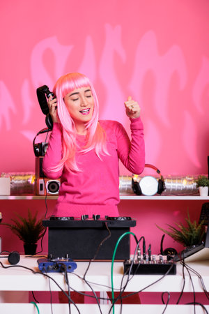 Asian musician dancing while playing electronic music at professional turntables while having fun with fans in club during night time. Dj artist performing song using professional audio equipmentの写真素材